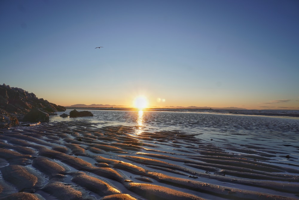 the sun is setting over the water at the beach