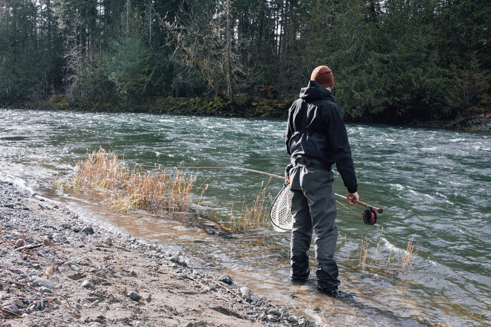 a man standing on a river bank holding a fish