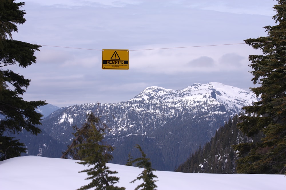 a yellow sign hanging from a wire above a snow covered mountain