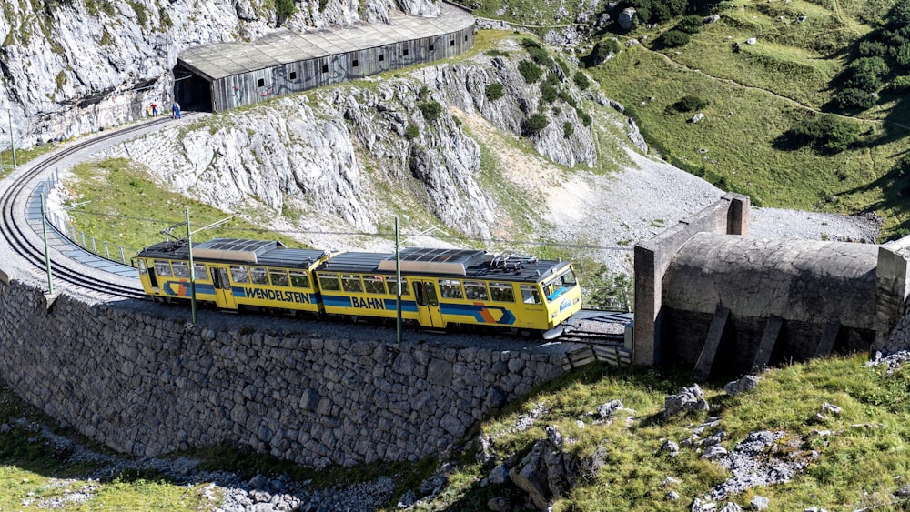 a yellow train traveling down train tracks next to a mountain