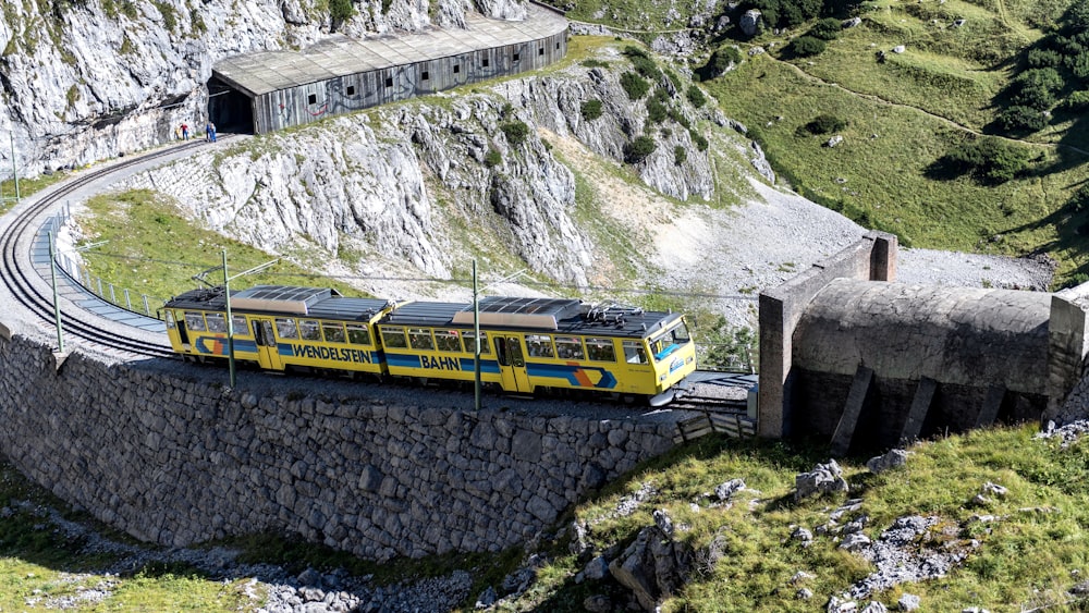 un treno giallo che viaggia lungo i binari del treno accanto a una montagna