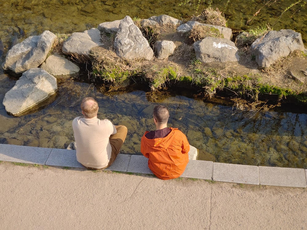 two men sitting on the edge of a river