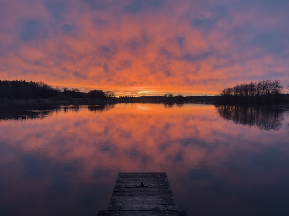 a dock sitting on top of a lake under a colorful sky