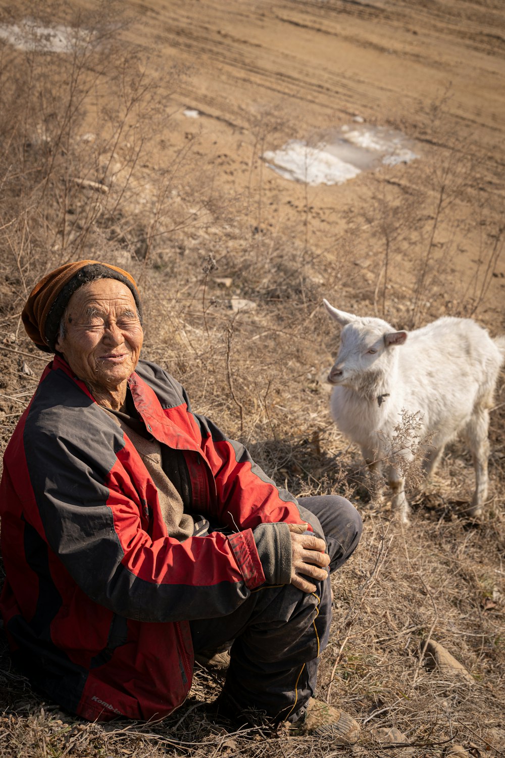 a man sitting in a field next to a goat