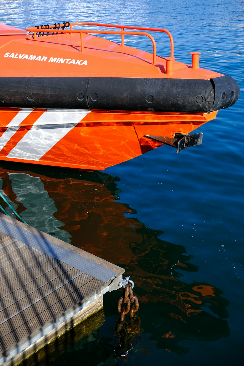 an orange boat in the water next to a dock