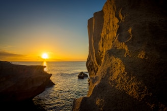 the sun is setting over the ocean from a cliff