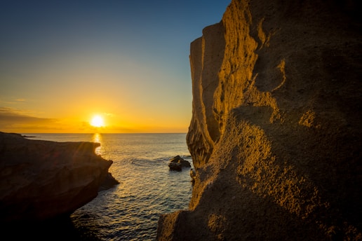 the sun is setting over the ocean from a cliff