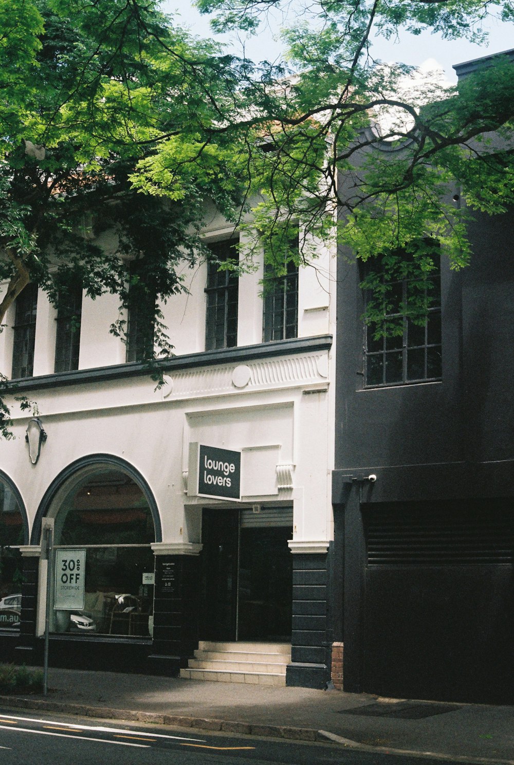 a tall white building sitting next to a lush green tree