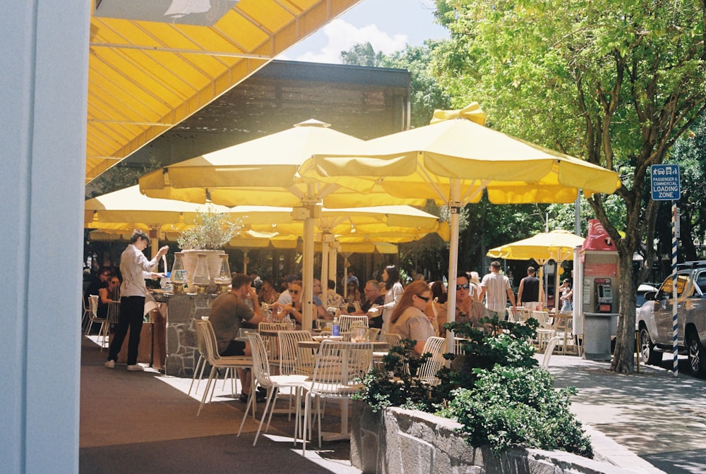 a group of people sitting at tables under yellow umbrellas