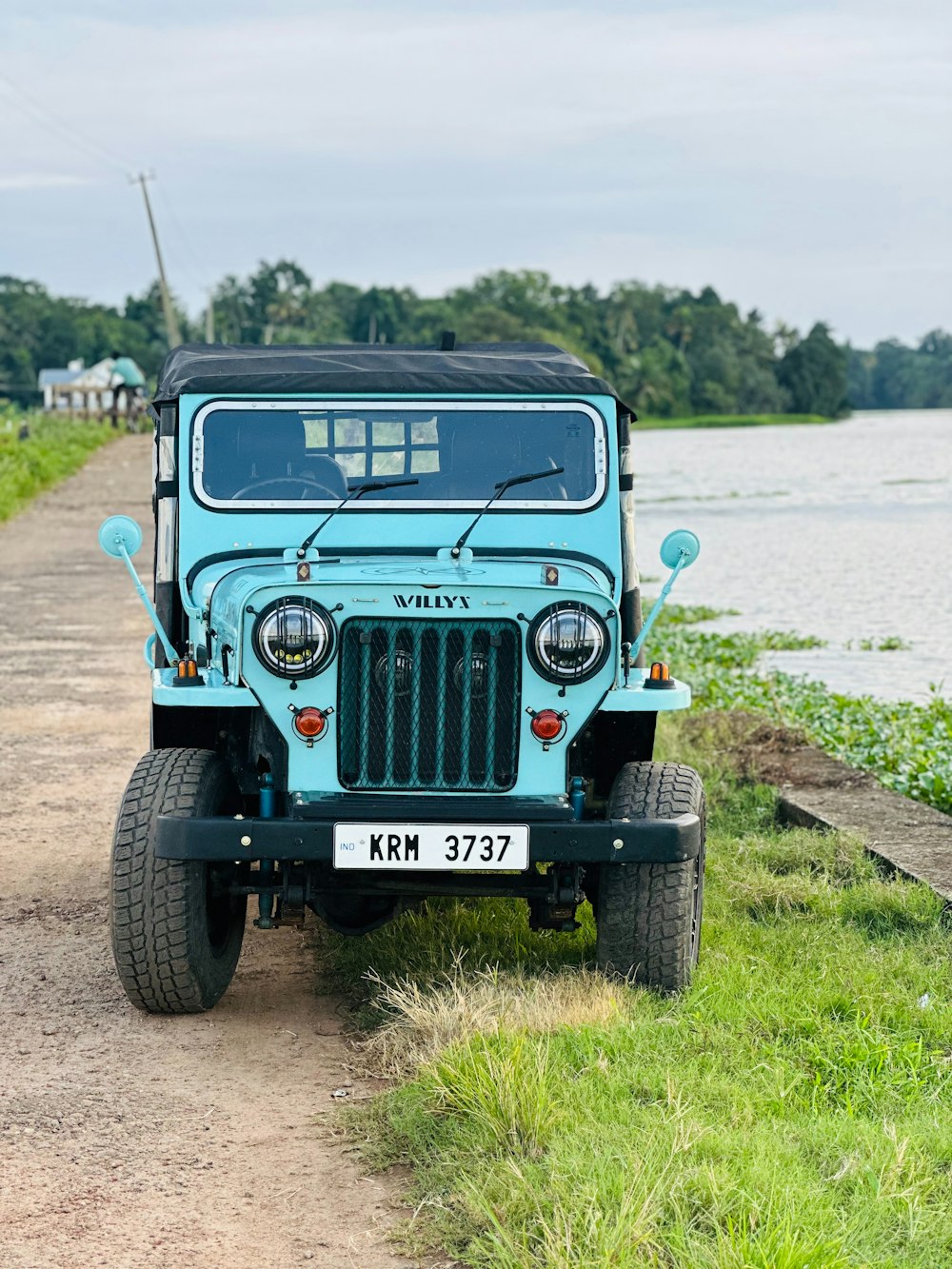 a blue jeep parked on a dirt road next to a body of water