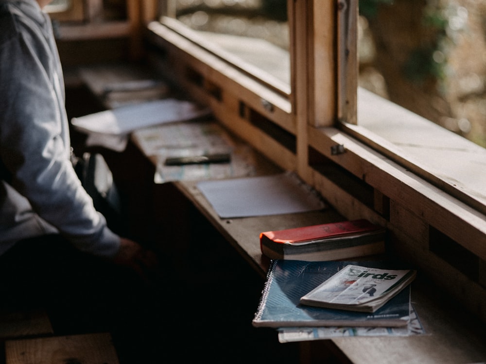 a man sitting at a window sill next to a stack of books