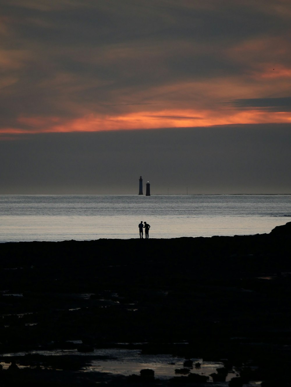 a couple of people standing on top of a beach next to the ocean