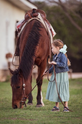 a little girl standing next to a brown horse