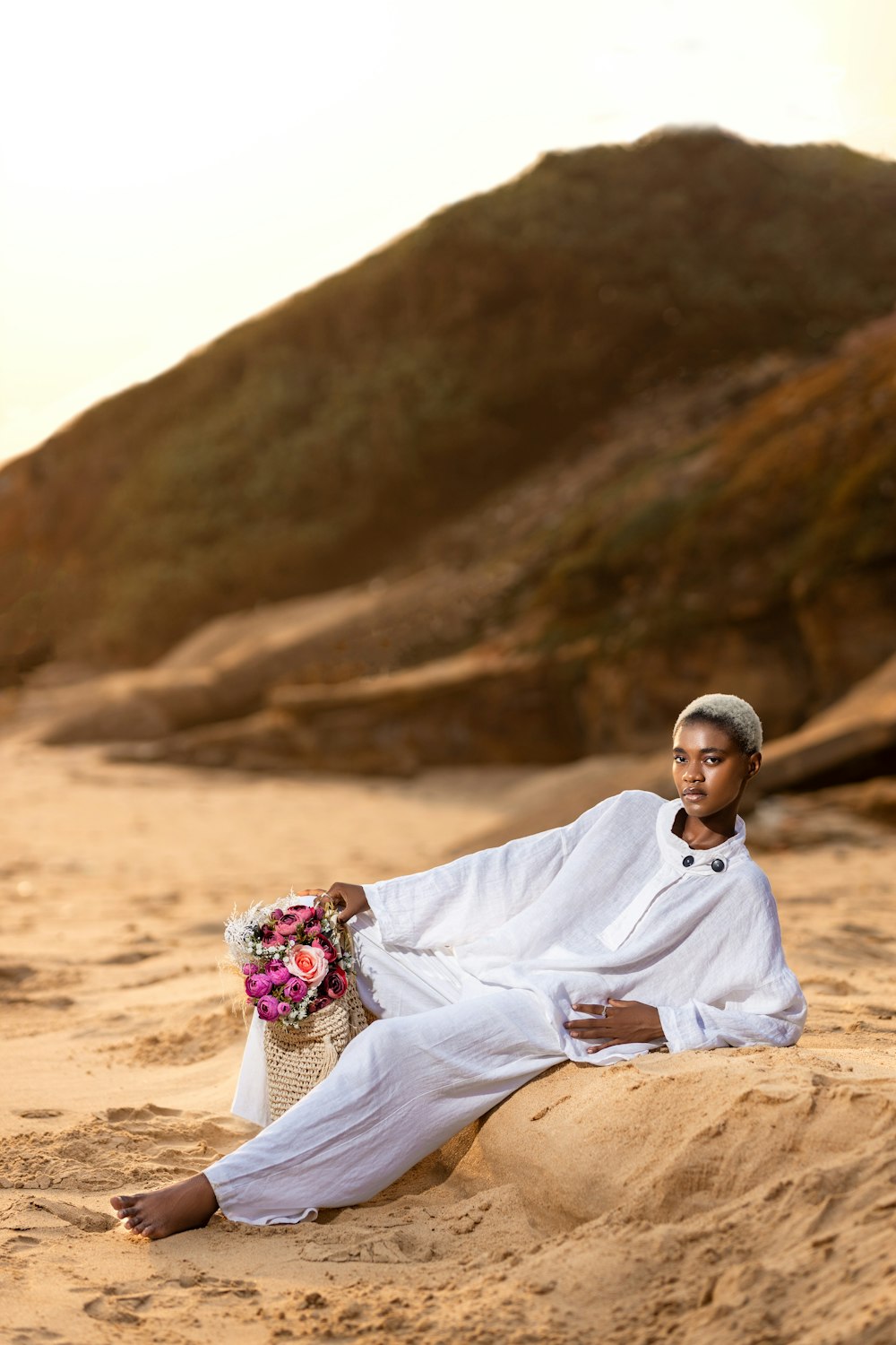 a man sitting in the sand holding a bouquet of flowers