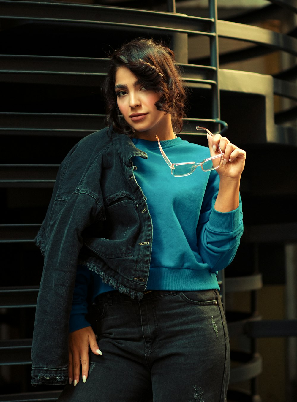 a woman in a blue shirt and jean jacket smoking a cigarette