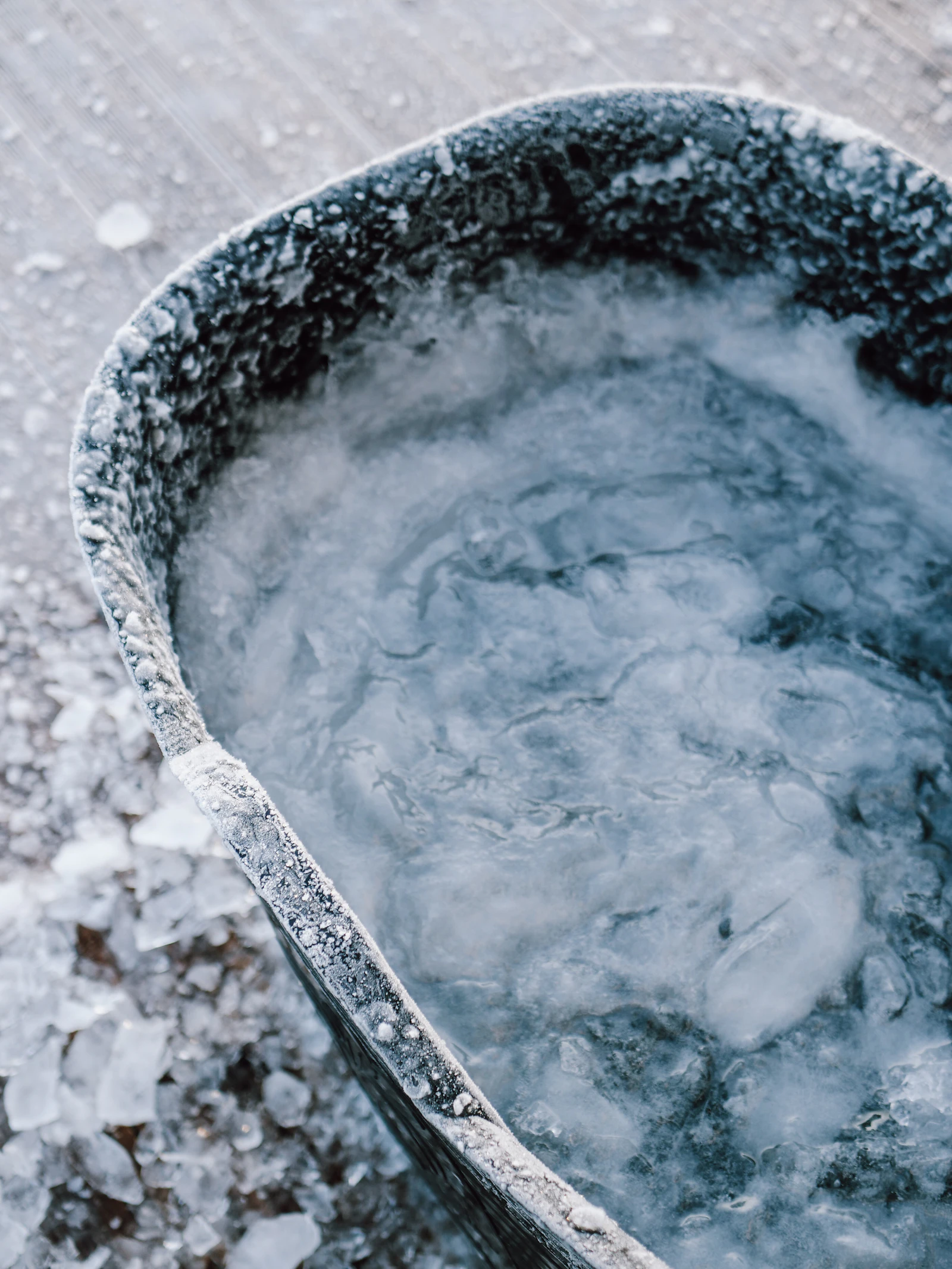 A battered metal tub filled with slush and floating ice, broken ice scattered across the ground beside it