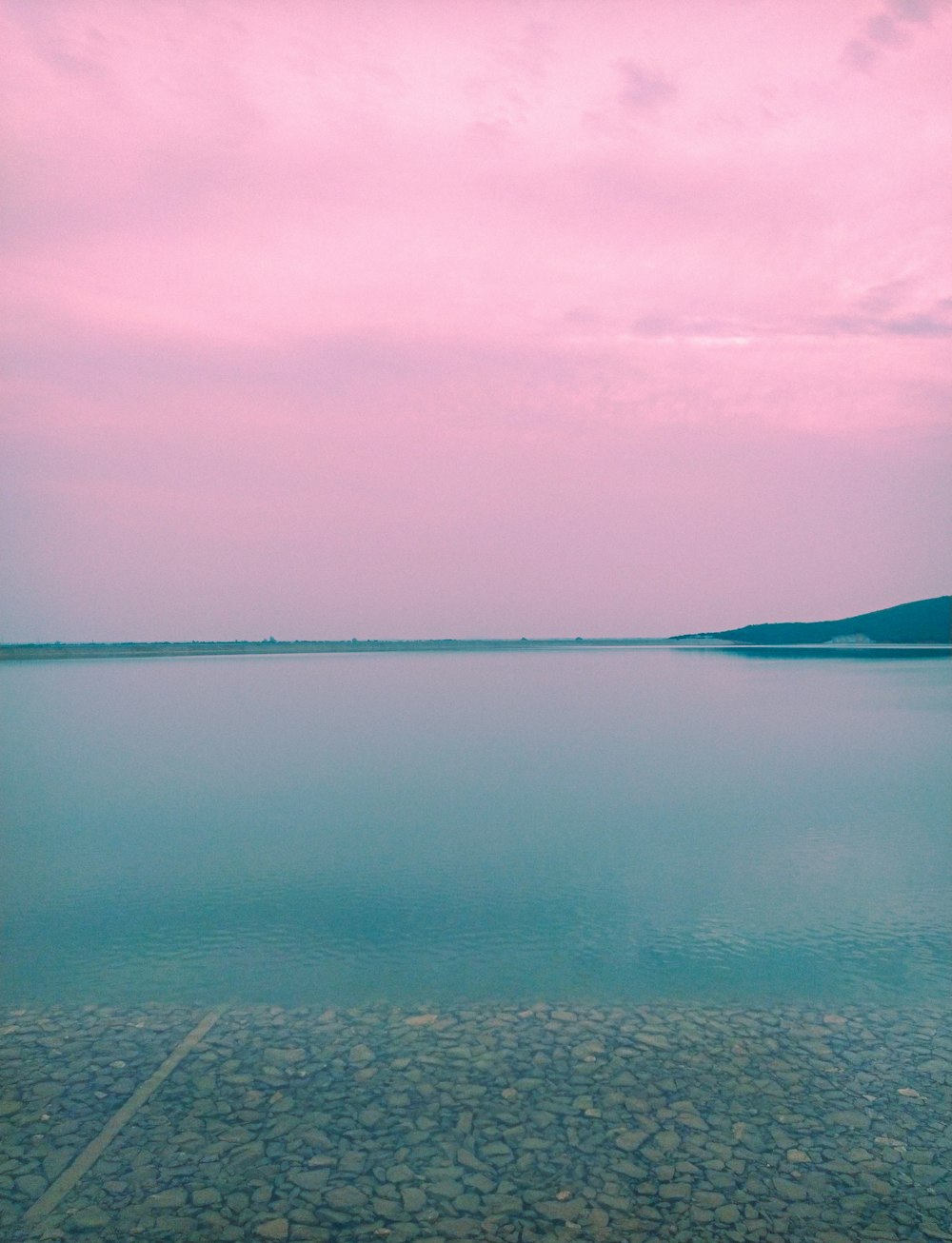 a large body of water sitting under a pink sky