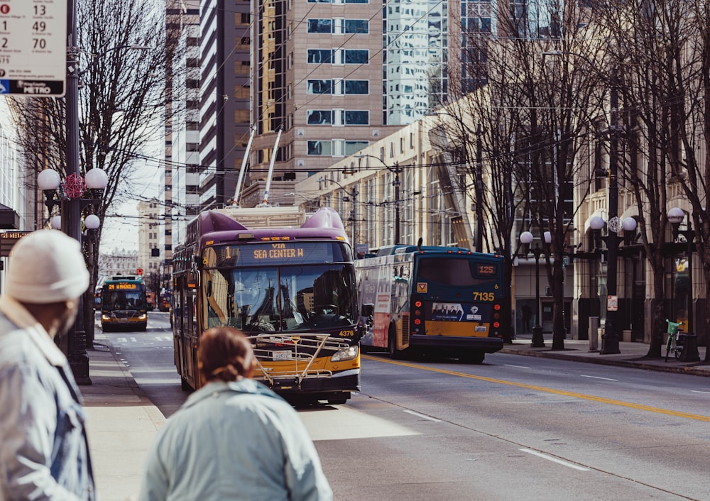 a couple of buses driving down a street next to tall buildings