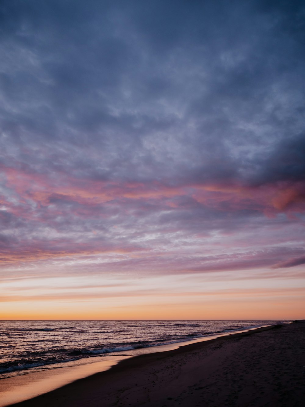 a sunset on the beach with clouds in the sky