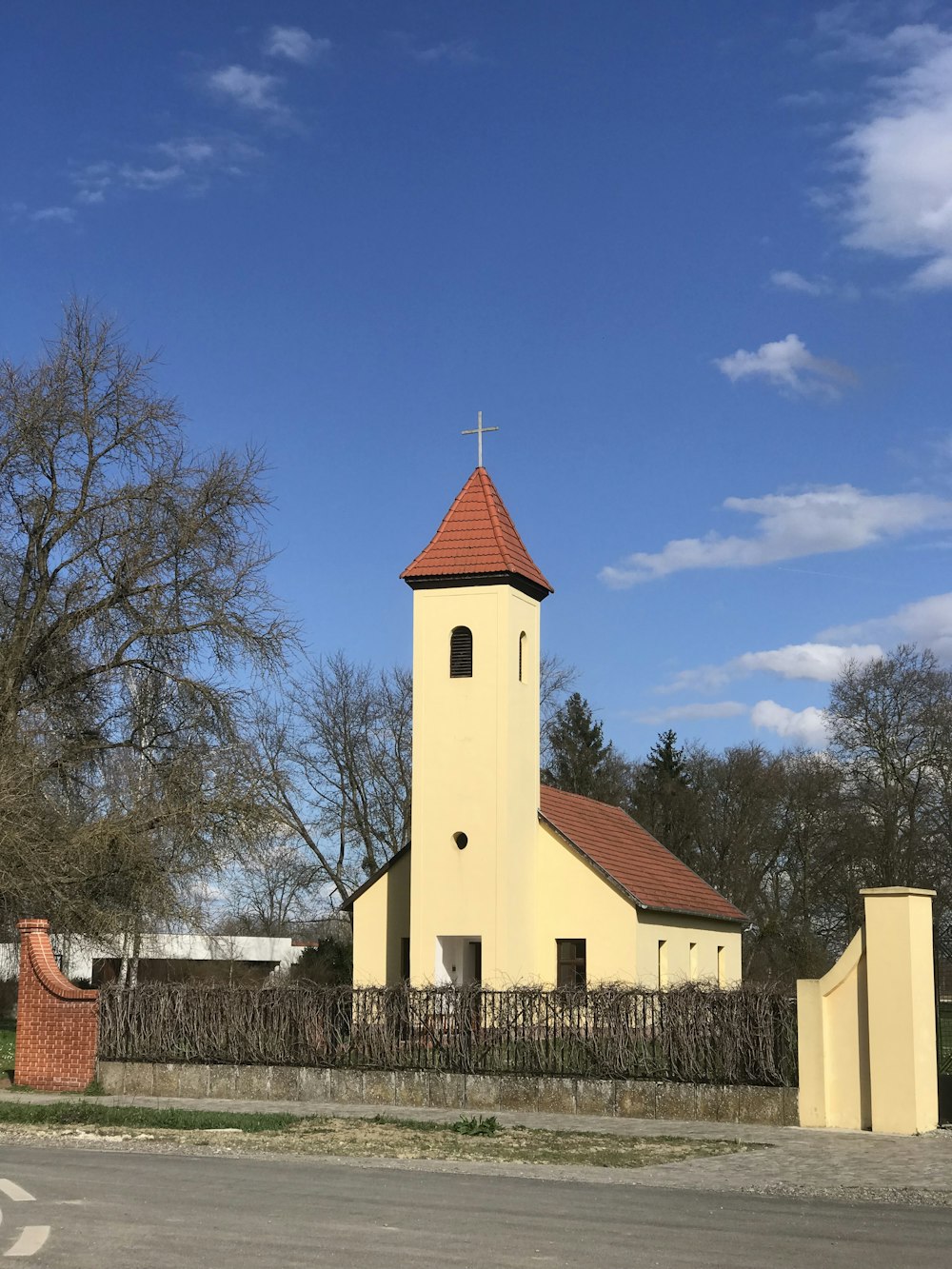 a yellow church with a red roof and a fence