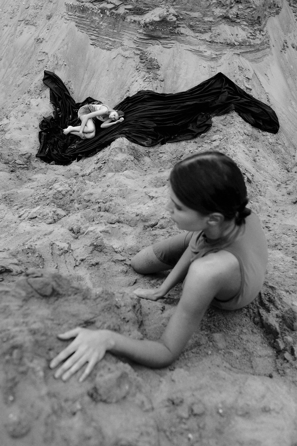 a woman laying on top of a sandy beach next to a body of water