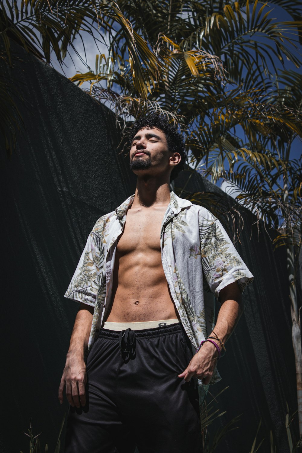 a shirtless man standing in front of a palm tree