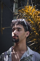 a man with a beard and sunglasses standing in front of a tree