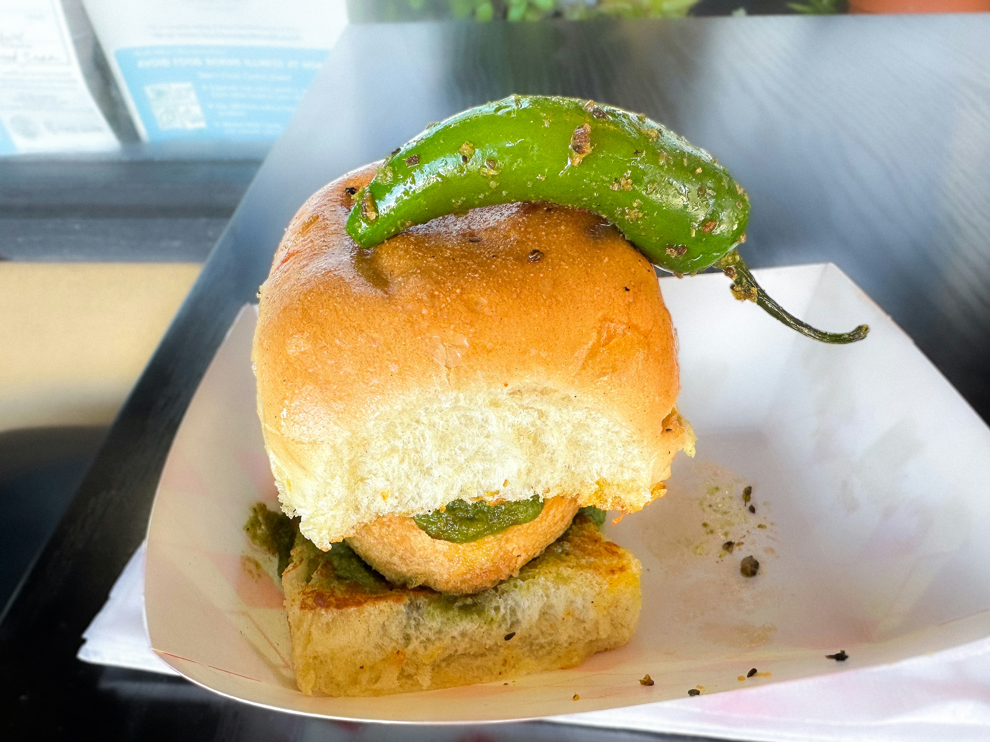 Vada pav with green and tamarind chutney on a dark plate, street food aesthetic