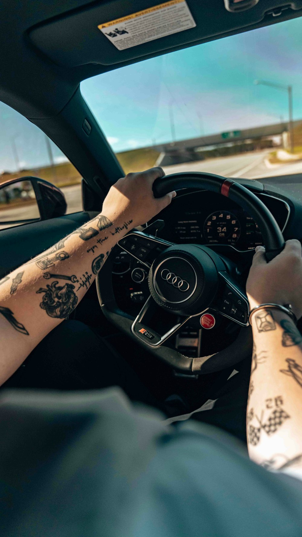 a man driving a car with tattoos on his arm