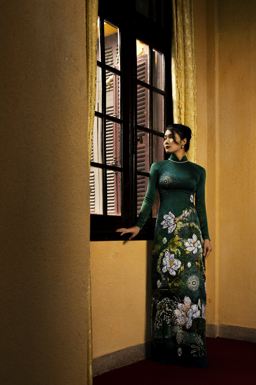 a woman in a green dress standing by a window