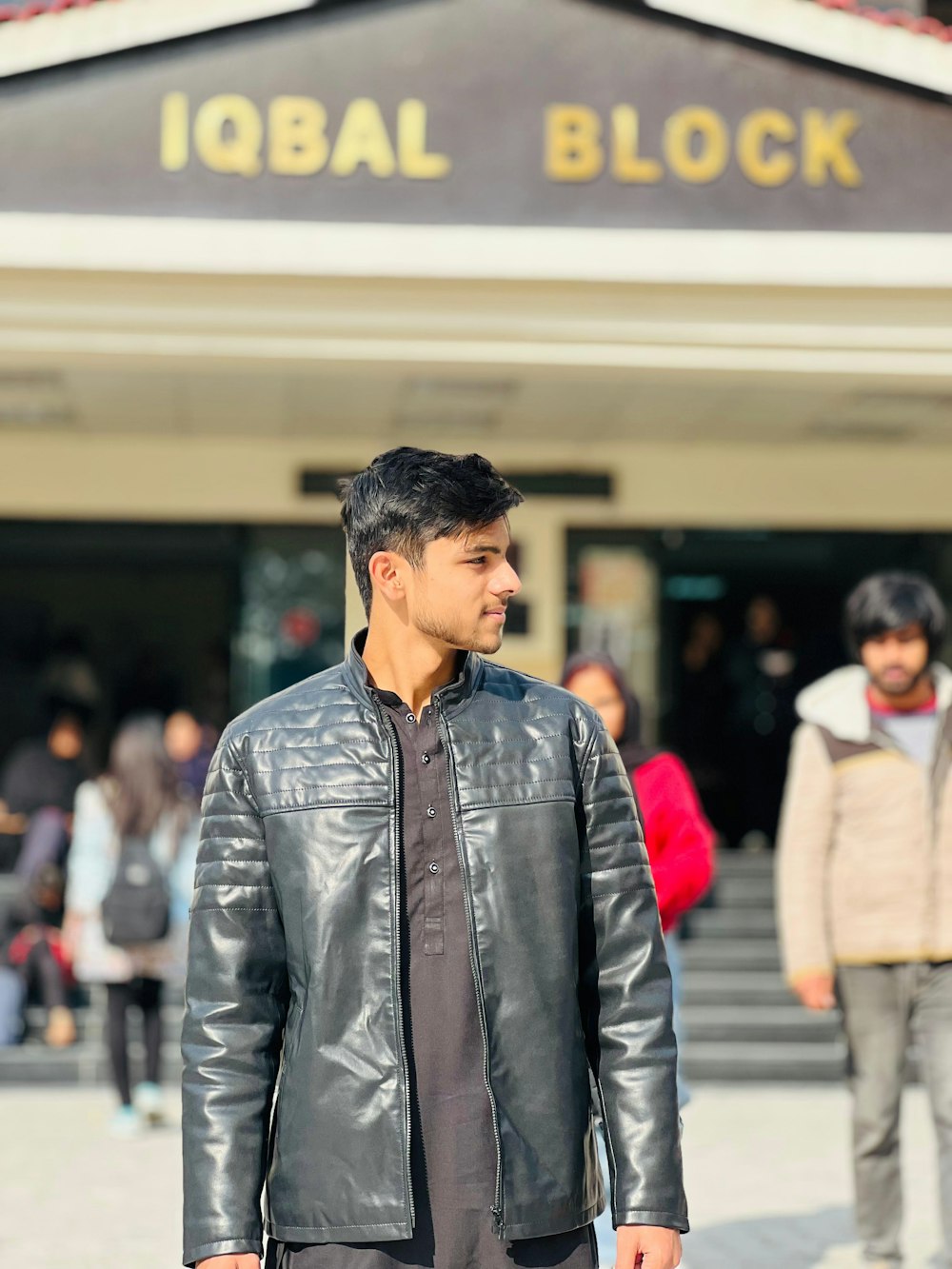 a man in a black leather jacket is standing in front of a building