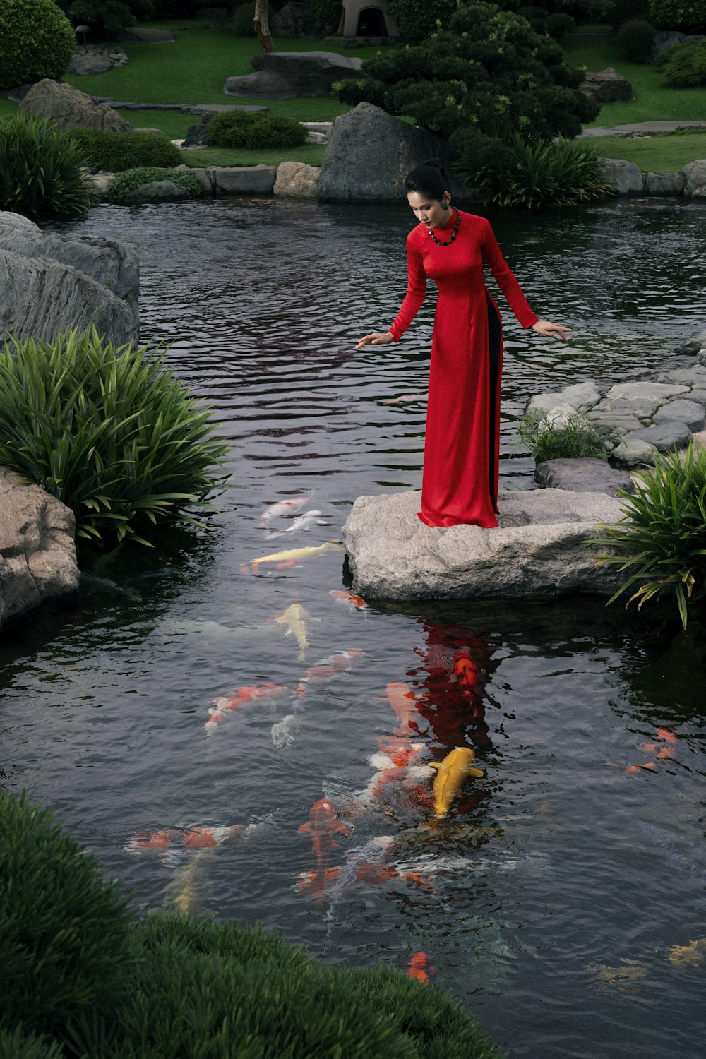 a woman in a red dress standing on a rock in a pond