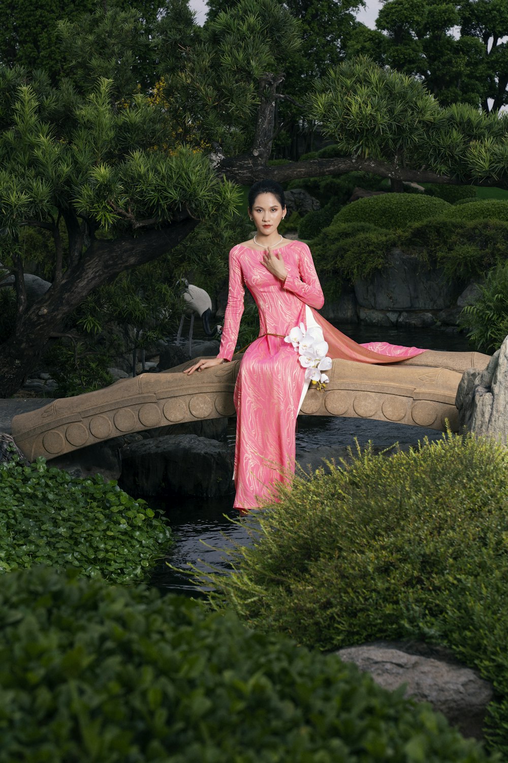 a woman in a pink dress sitting on a bridge