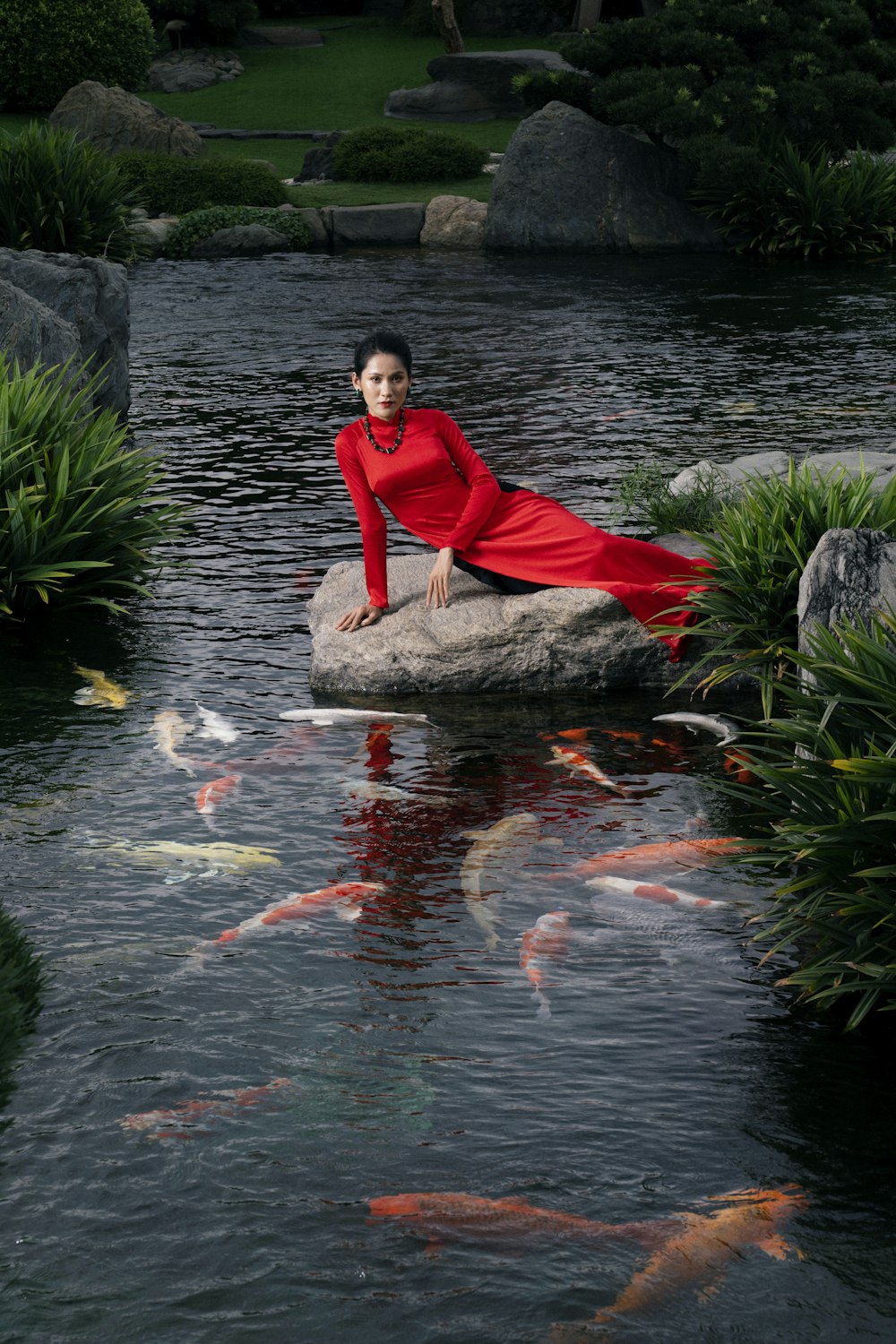 a woman in a red dress sitting on a rock in a pond