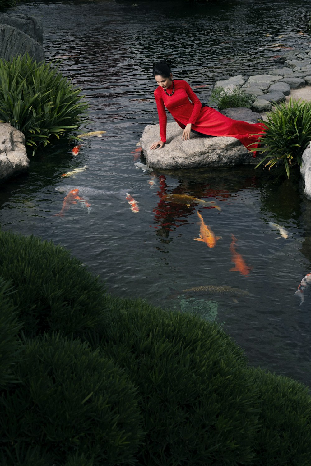 a woman in a red dress sitting on a rock in a pond