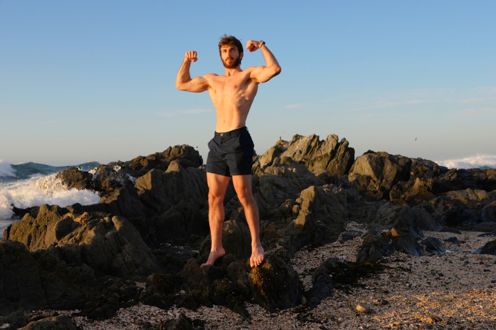 a man standing on top of a rocky beach next to the ocean