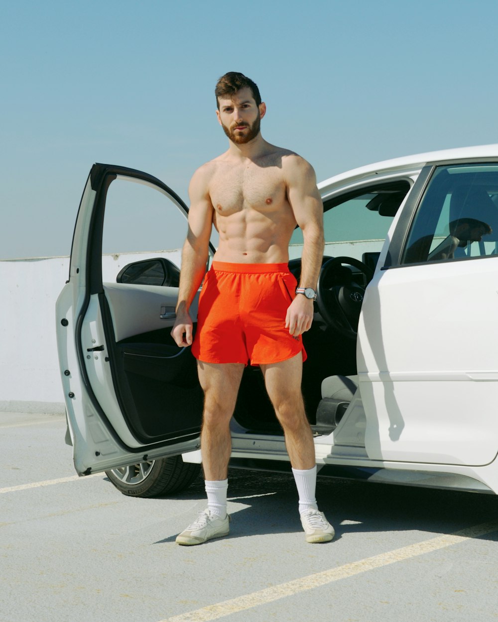 a shirtless man standing in front of a white car