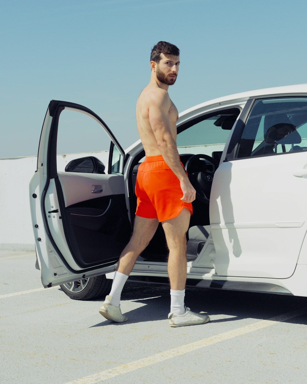 a man in orange shorts stepping out of a white car