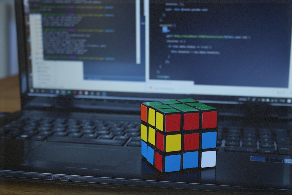 a rubik cube sitting on top of a laptop computer