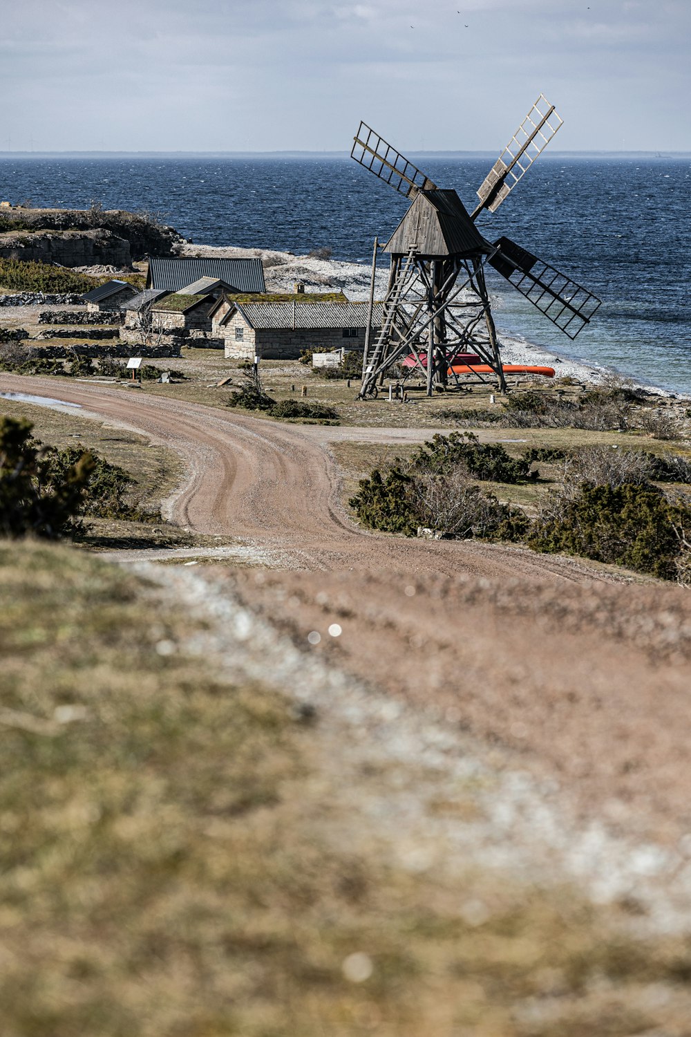 a windmill on the side of a dirt road next to the ocean