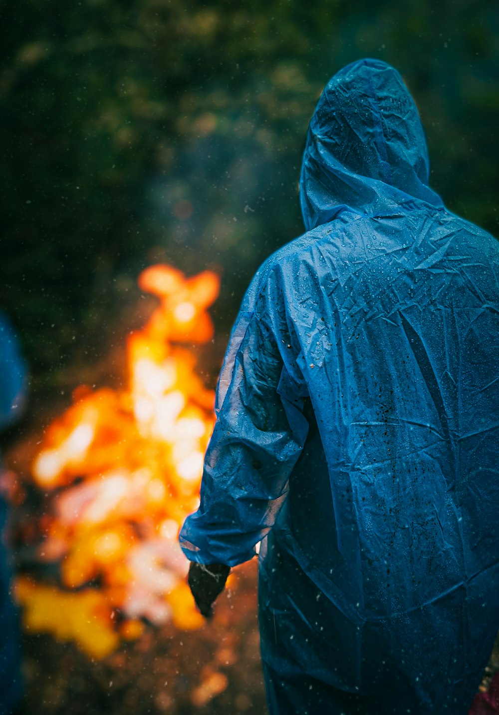 a person in a blue rain coat standing in front of a fire