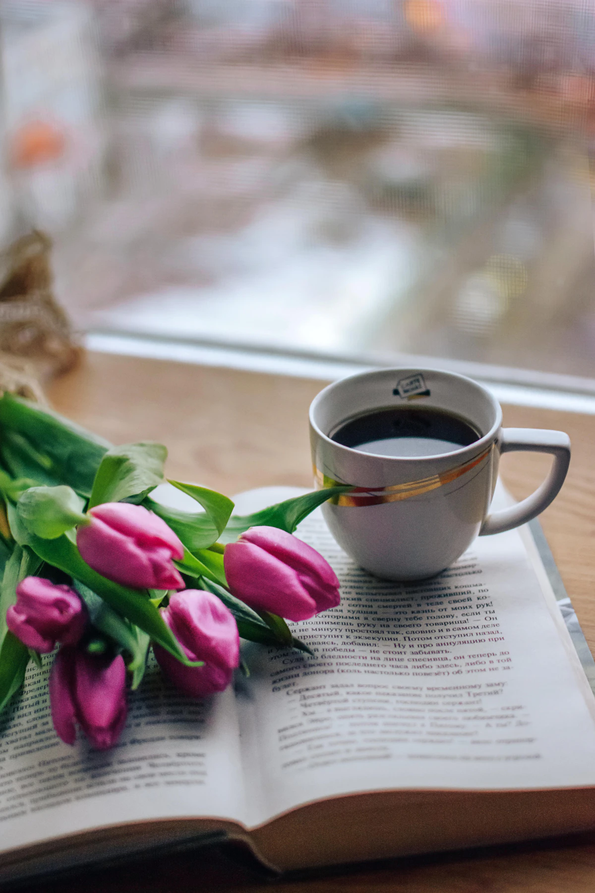 A cup of coffee beside pink tulips on a table