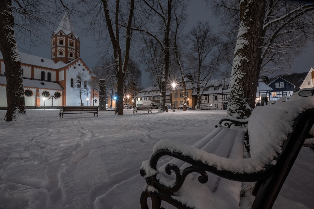 a bench covered in snow in front of a church