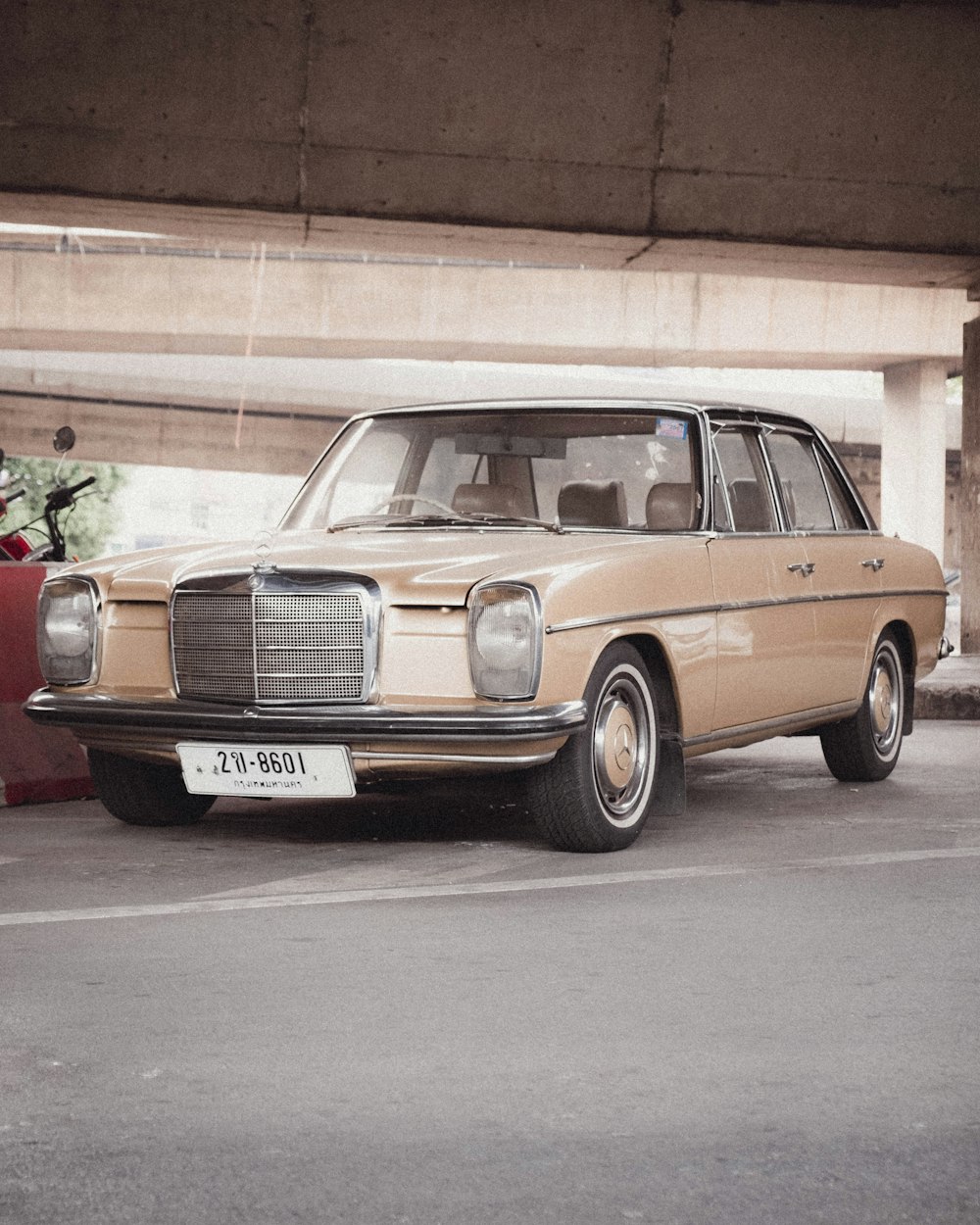 a tan car parked in a parking lot under a bridge