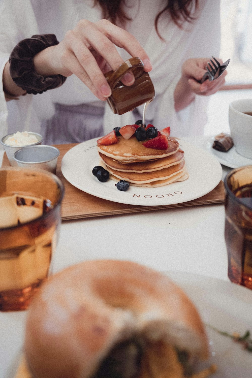 a woman is pouring syrup on a stack of pancakes
