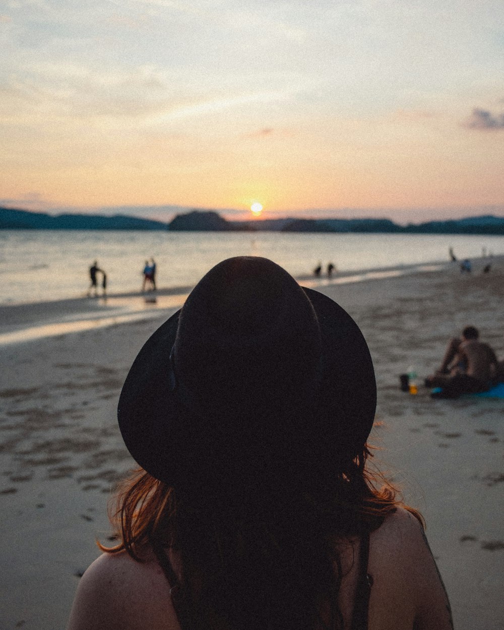 una donna che indossa un cappello in piedi in cima a una spiaggia