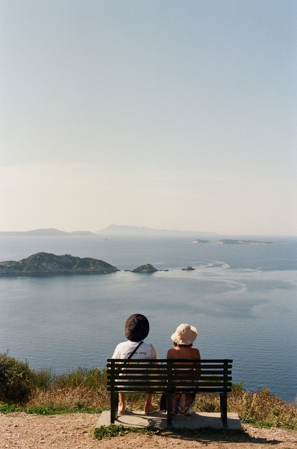 two people sitting on a bench looking out at the water