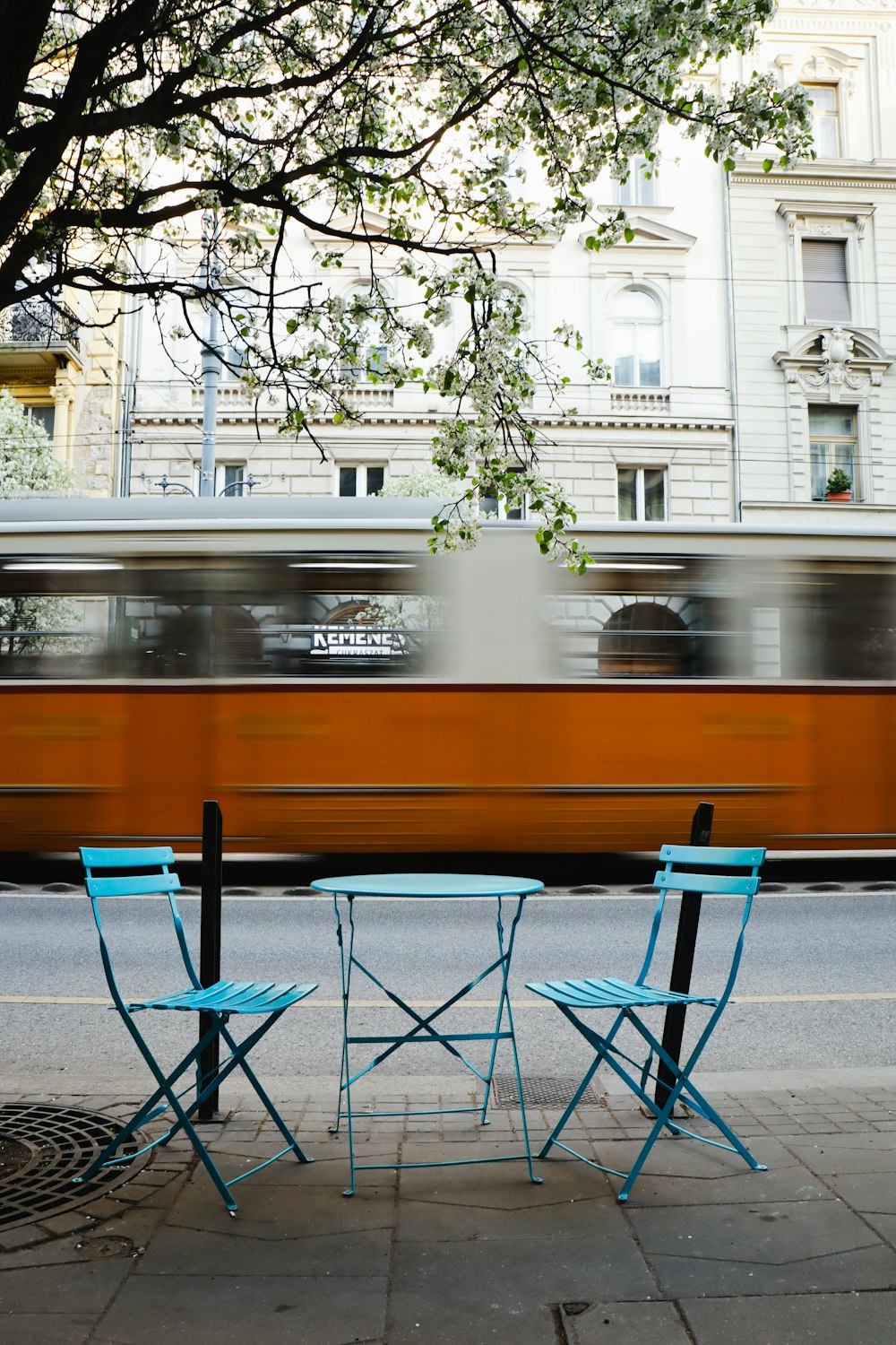 two chairs and a table on a sidewalk with a train passing by