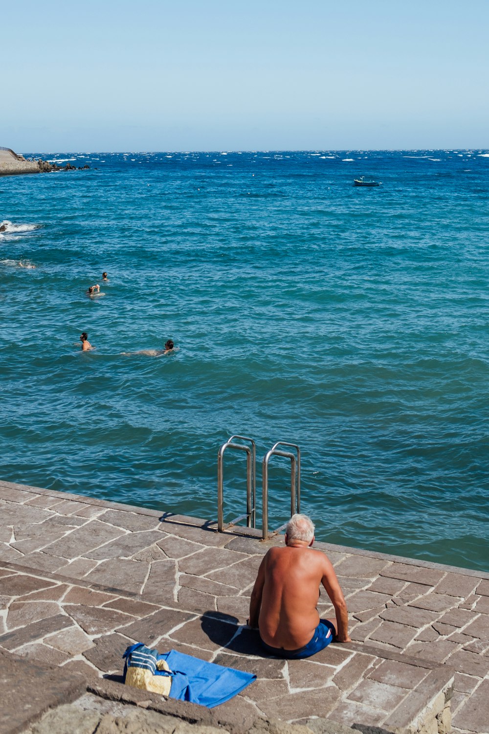 a man sitting on the edge of a pier next to the ocean