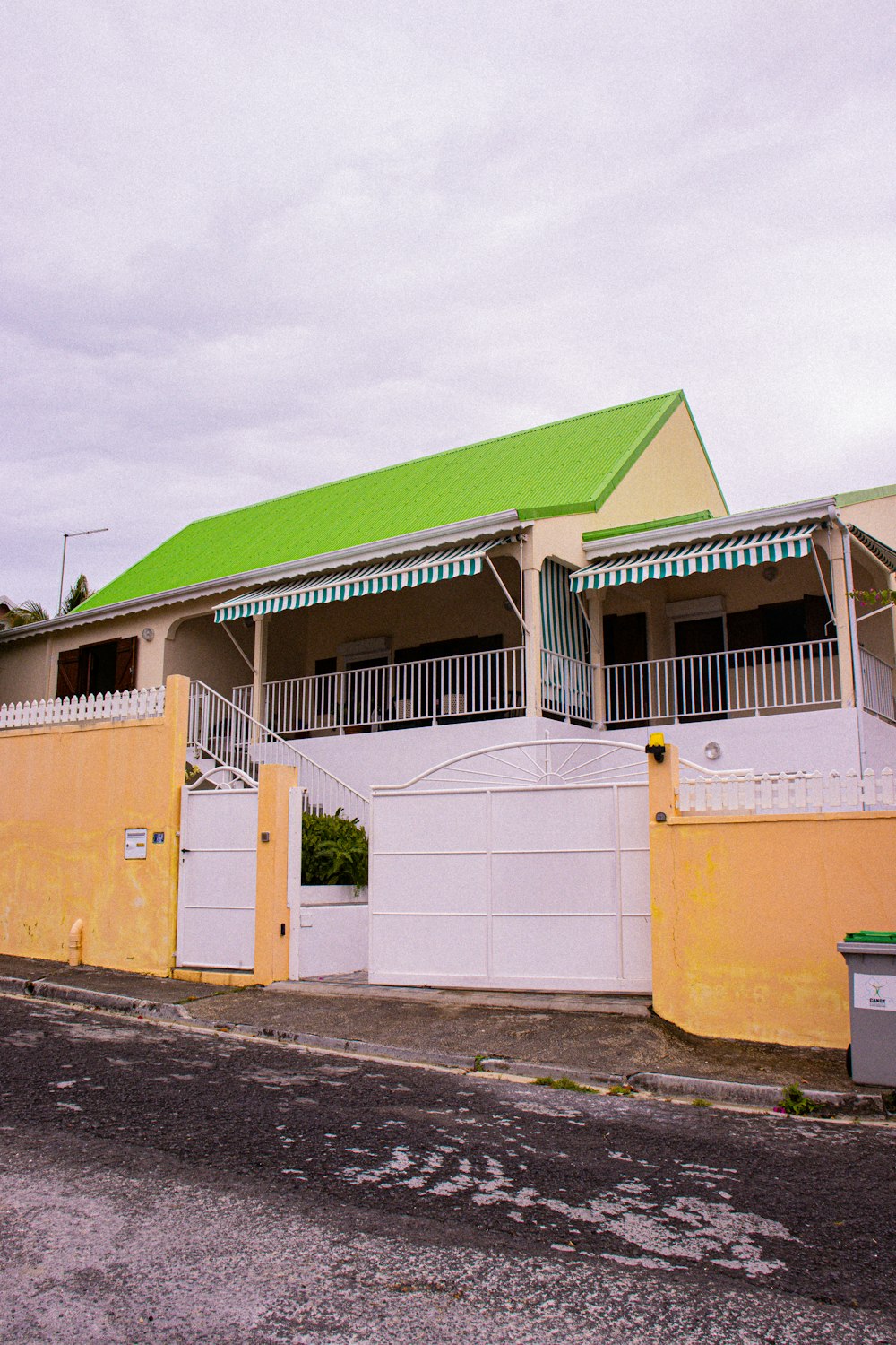 a yellow house with a green roof and a white fence